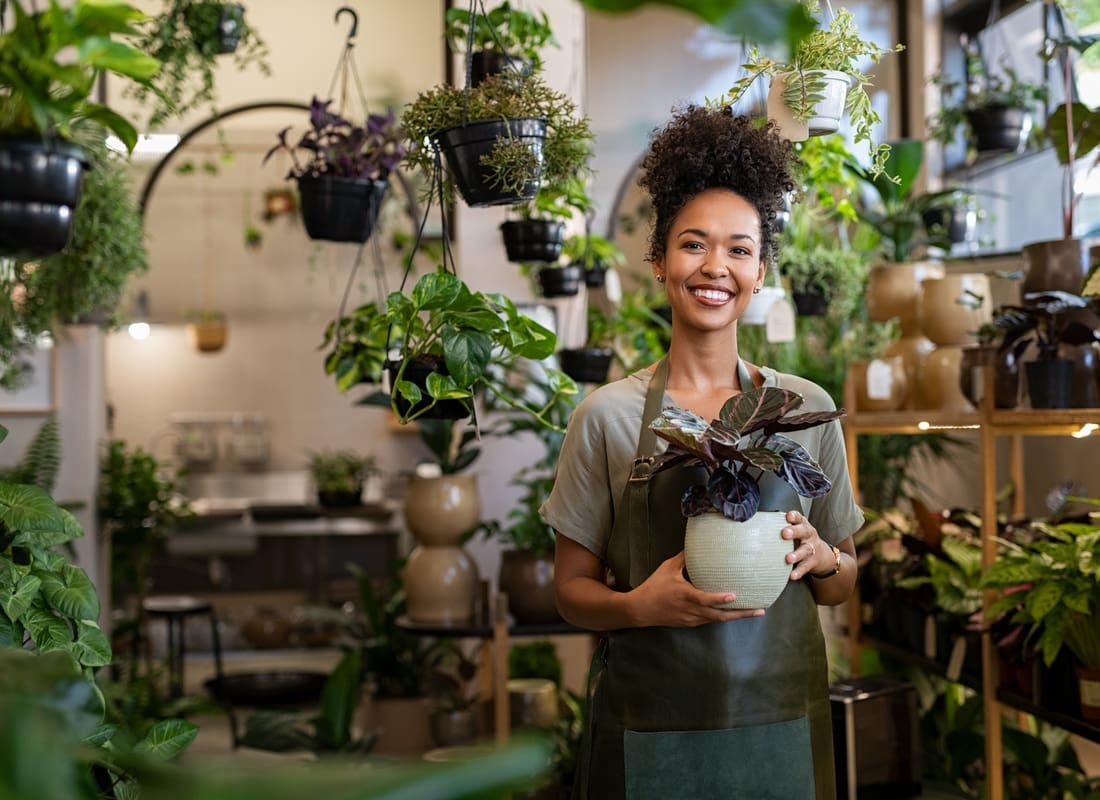 Business Insurance - Smiling Woman Holding a Potted Plant in a Lush Plant Shop